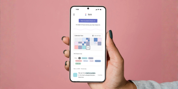 A woman holding up a phone with the Habit app calendar view which shows how often the user has reflected, benefiting from the visual cue effect to support self-care consistency.