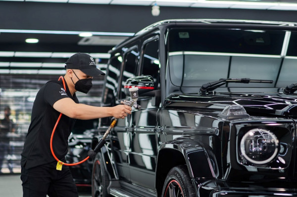 A person in a black shirt and black hat holding an object to a black vehicle

Description automatically generated